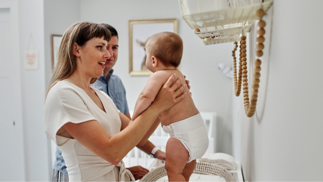 Mom smiling while holding baby on changing table while standing next to dad.